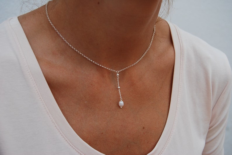 Puede incluir: Un delicado collar de cadena de plata con un solo colgante de perla. La cadena es simple, fina y la perla es peque&ntilde;a y blanca.