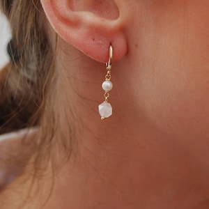 May include: Gold dangle earrings with a white pearl and a faceted white gemstone.