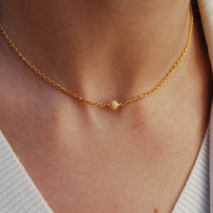 Puede incluir: Un delicado collar de cadena de oro con un pequeño colgante de cuentas de oro texturizado.