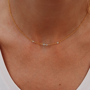 May include: A gold chain necklace with small white beads. The necklace is delicate and simple.