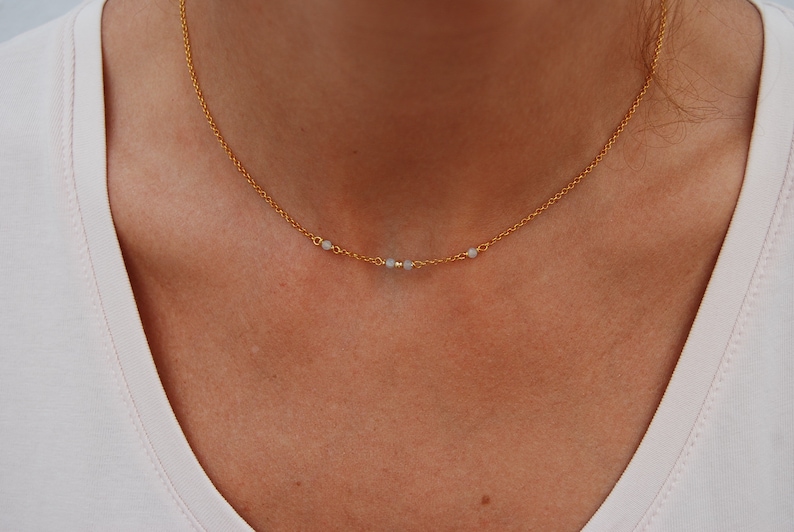 May include: A gold chain necklace with small white beads. The necklace is delicate and simple.