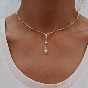 Puede incluir: Un collar de cadena de plata con un colgante de perla &uacute;nico. La cadena es delicada y la perla es peque&ntilde;a y blanca.