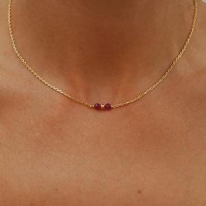 Peut inclure: Un collier délicat en chaîne dorée avec deux petites perles de pierres précieuses rouge foncé.