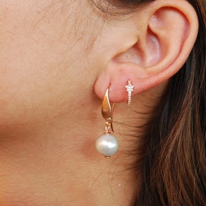 May include: A pair of earrings featuring a large, off-white pearl dangling from a gold hook and a smaller gold hoop earring with a star-shaped diamond cluster.