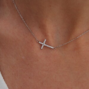 Puede incluir: Un collar de cadena de plata con un pequeño colgante de cruz engastado con diamantes.