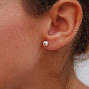 May include: A close-up of a person's ear with a small pearl earring with a gold star in the center.