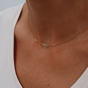 May include: A gold chain necklace with three small white beads.