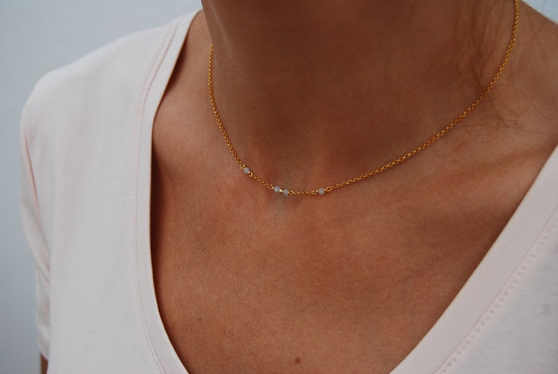 May include: A gold chain necklace with three small white beads.