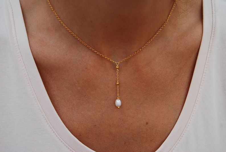 Puede incluir: Un collar de cadena dorada con un colgante de perla &uacute;nico. La cadena es delicada y presenta peque&ntilde;as cuentas doradas.