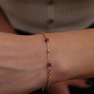 Peut inclure: Un bracelet délicat en chaîne dorée avec trois petites perles rouge rubis.