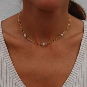 May include: A gold chain necklace with three small white pearls. The necklace is on a person's neck.