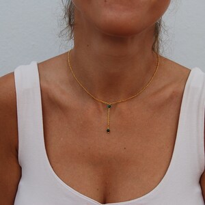 May include: A gold chain necklace with two small green gemstone beads hanging from it.