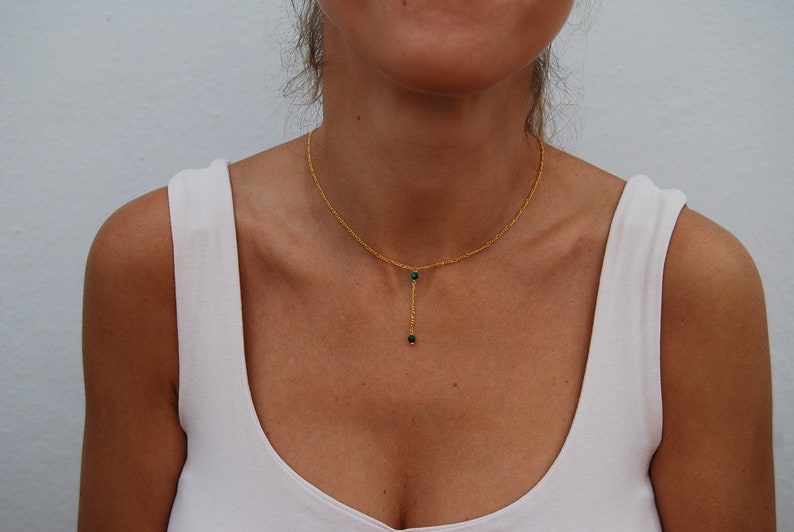 May include: A gold chain necklace with two small green gemstone beads hanging from it.