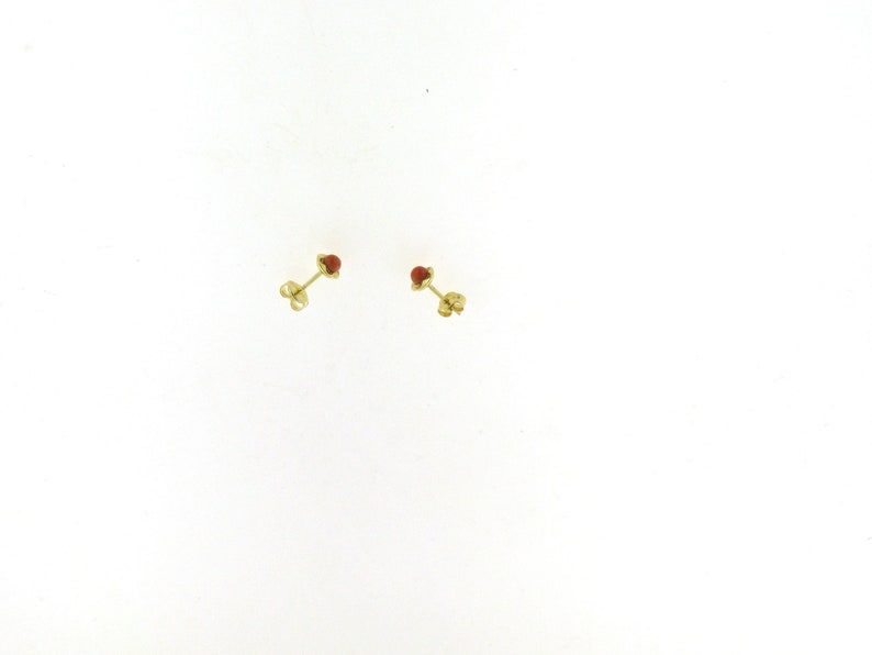 May include: A pair of gold stud earrings with small red gemstone accents.
