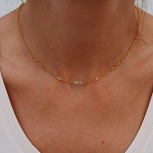 May include: A delicate gold chain necklace with three small white beads.