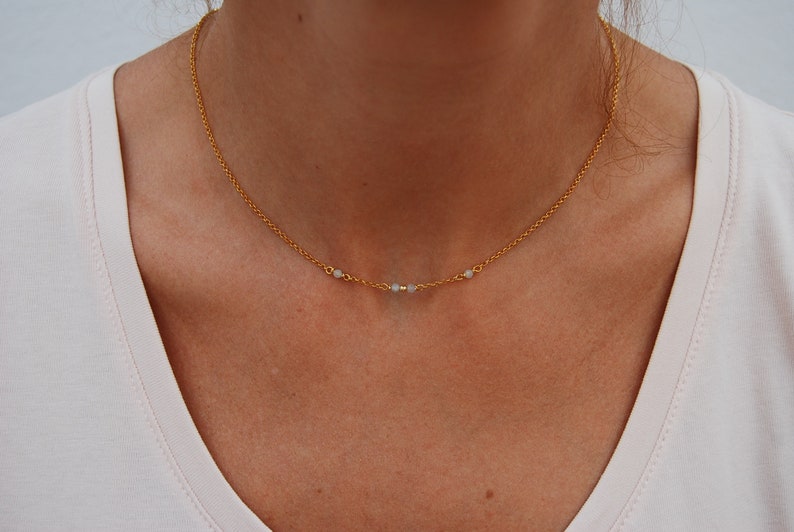 May include: A delicate gold chain necklace with three small white beads.