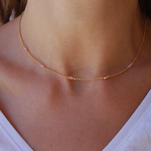 Op de afbeelding: Een delicate gouden ketting met kleine roze kralen. De ketting is een eenvoudig en elegant sieraad.
