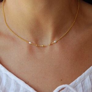 Op de afbeelding: Een delicate gouden ketting met twee kleine parel accenten en drie gouden kralen.