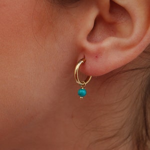 Op de afbeelding: Gouden creolen met een turquoise steen die eronder hangt.