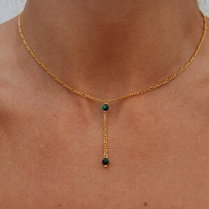 May include: A gold chain necklace with a green stone pendant. The pendant is a long, thin chain with two green stones at the end.