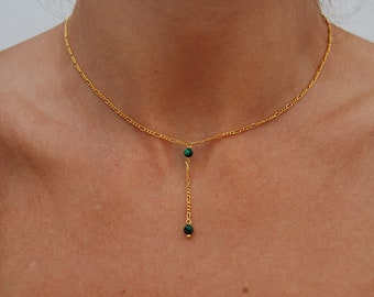 May include: A gold chain necklace with a green stone pendant. The pendant is a long, thin chain with two green stones at the end.