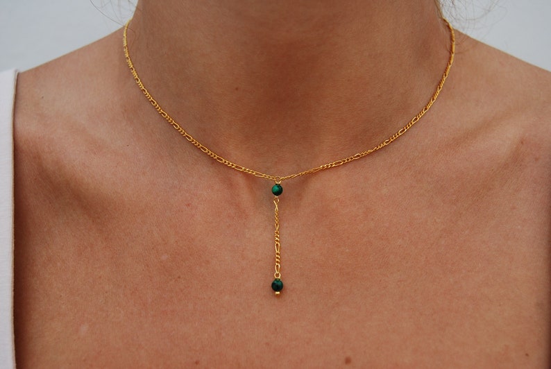 May include: A gold chain necklace with a green stone pendant. The pendant is a long, thin chain with two green stones at the end.