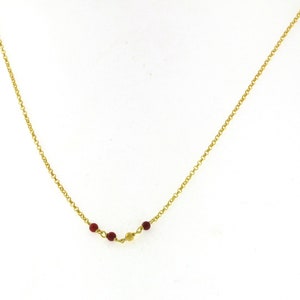 May include: A delicate gold-colored necklace featuring a series of small, round, red beads and a single gold-colored bead. The beads are strung along a fine chain, creating a subtle and elegant design. The necklace is displayed against a white background.