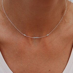 May include: A silver chain necklace with three small, light blue beads.