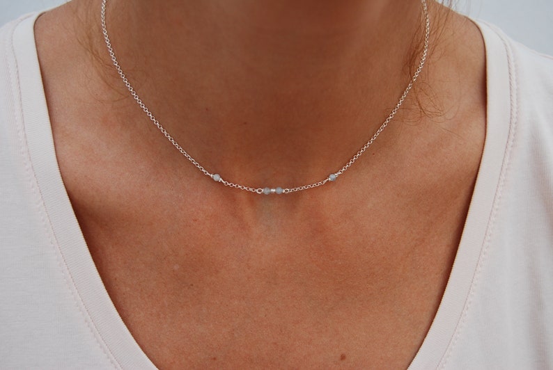 May include: A silver chain necklace with three small, light blue beads.