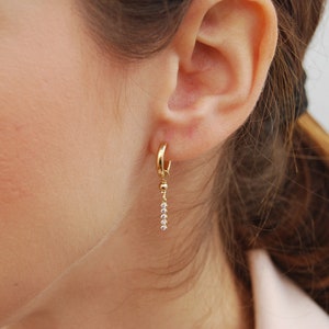 May include: Gold hoop earrings with a dangling chain of small clear stones.