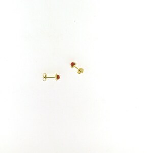 May include: A pair of gold stud earrings with small red gemstone accents.