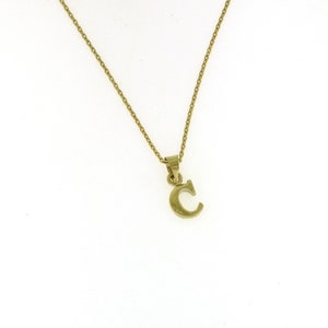 Puede incluir: Un collar de cadena de oro con un colgante de letra C de oro.