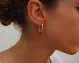May include: Gold hoop earrings with a small red bead dangling from the bottom.