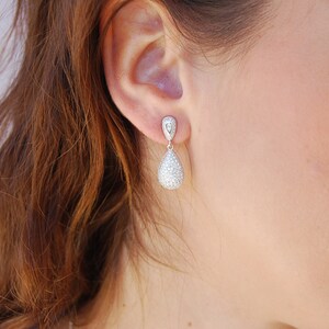 May include: Silver teardrop earrings with a clear crystal design. The earrings are dangling from the earlobe.