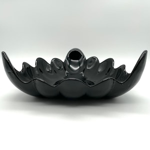 May include: A glossy black decorative bowl with a unique, petal-like design. The bowl has a central, circular indentation and a series of curved, wave-like edges. The bowl is made of a shiny, reflective material.