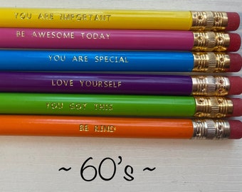 May include: Six colorful pencils with inspirational messages in gold lettering. The pencils are yellow, pink, blue, purple, green, and orange. The messages are "You are important", "Be awesome today", "You are special", "Love yourself", "You got this", and "Be kind". The pencils are arranged in a row on a white surface. The text "~60's~" is written below the pencils.