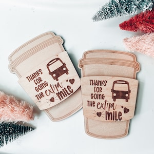 May include: Two wooden coffee cup sleeves with the text "Thanks for going the extra mile" and a small bus graphic. Each sleeve has two small hearts.