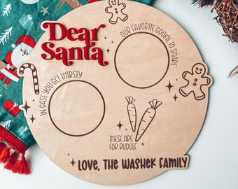May include: A round wooden plate with the words "Dear Santa" in red lettering. The plate has three circles for placing treats, with the text "Our favorite cookie to share", "In case you get thirsty", and "These are for Rudolph". The plate also has a gingerbread man graphic and the text "Love, The Washek Family".