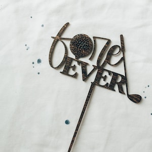 May include: A brown wooden cake topper with the words "Golf Ever" and a golf ball design.