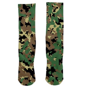 Op de afbeelding: Twee kniehoge sokken met een gepixeld camouflagepatroon in groen, bruin en zwart. De sokken worden gepresenteerd tegen een witte achtergrond, waarbij de volledige lengte en het ontwerp worden getoond.