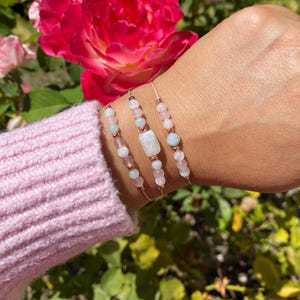 May include: Three delicate bracelets with rose gold accents and light blue and pink gemstone beads. The bracelets are stacked on a wrist.