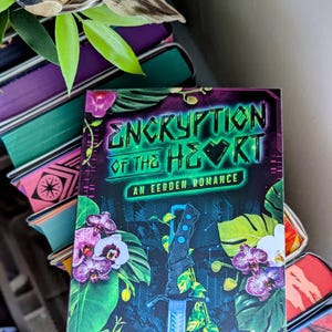 May include: A book cover with a dark background and a neon green title that reads "Encryption of the Heart". The cover also features a silver sword, green leaves, and white orchids.