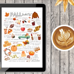 May include: A digital tablet shows a fall bucket list with watercolour illustrations of autumn activities. A cup of coffee with latte art and autumn leaves are on a wooden surface. The list includes activities like apple picking and making pumpkin pie.