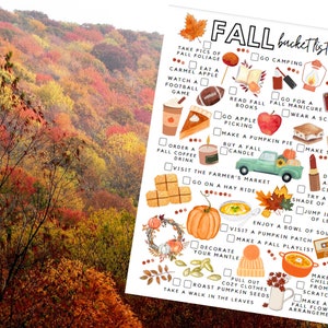 May include: A seasonal print with a "Fall Bucket List" featuring illustrations of autumn activities. The list includes things like apple picking, pumpkin pie, and cozy sweaters. The background shows a vibrant autumn forest with red, orange, and yellow foliage.