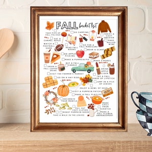 May include: A framed print with a gold-colored frame displays a fall bucket list with watercolor illustrations. The list includes activities like apple picking, visiting a pumpkin patch, and enjoying a bowl of soup. The words "FALL bucket list" are at the top.