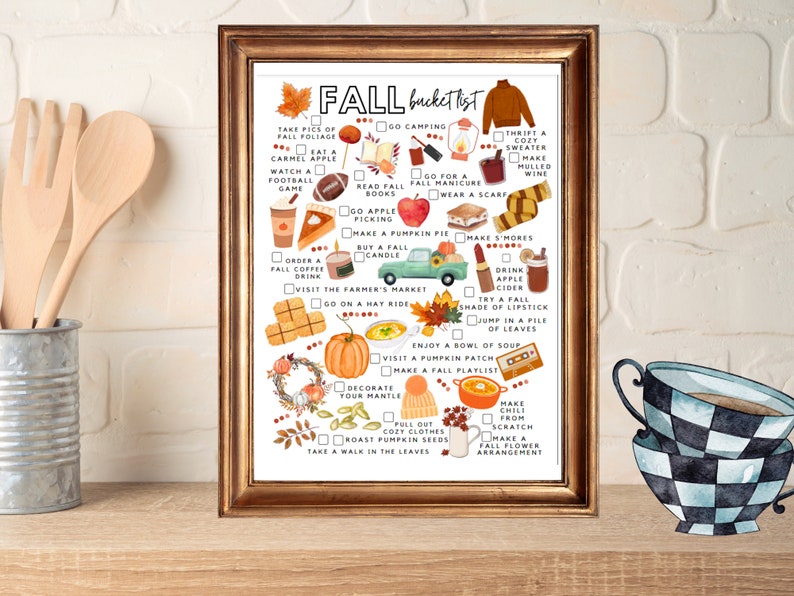 May include: A framed print with a gold-colored frame displays a fall bucket list with watercolor illustrations. The list includes activities like apple picking, visiting a pumpkin patch, and enjoying a bowl of soup. The words "FALL bucket list" are at the top.