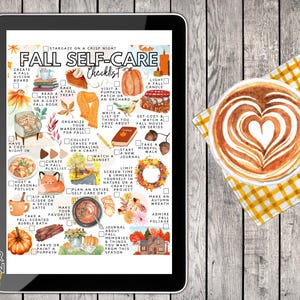 May include: A digital tablet displays a "Fall Self-Care Checklist" with autumn-themed illustrations and text. A latte with heart-shaped foam art sits on a yellow checkered napkin, next to the tablet on a wooden surface.