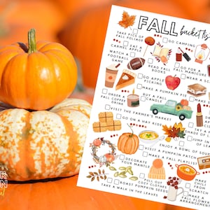May include: Two pumpkins, one on top of the other, are in front of a blurred background of more pumpkins. A printed "Fall Bucket List" is visible, featuring autumn-themed activities like apple picking and making pumpkin pie.