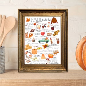 May include: A framed print titled "Fall Bucket List" in a gold-coloured frame. The list features autumn activities such as apple picking, wearing a scarf, and making s'mores. The print is decorated with autumn-themed illustrations and text.