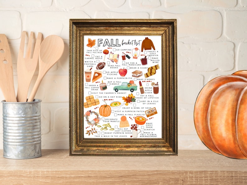 May include: A framed print titled "Fall Bucket List" in a gold-coloured frame. The list features autumn activities such as apple picking, wearing a scarf, and making s'mores. The print is decorated with autumn-themed illustrations and text.